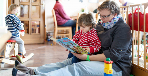 Familienarbeit im Kirchenkreis Neustadt-Wunstorf. Bild: P. Schroeder Familienarbeit im Kirchenkreis Neustadt-Wunstorf. Ehrenamtliche ließt Kind ein Buch vor. Mutter im Hintergrund im Geschäftsgespräch.